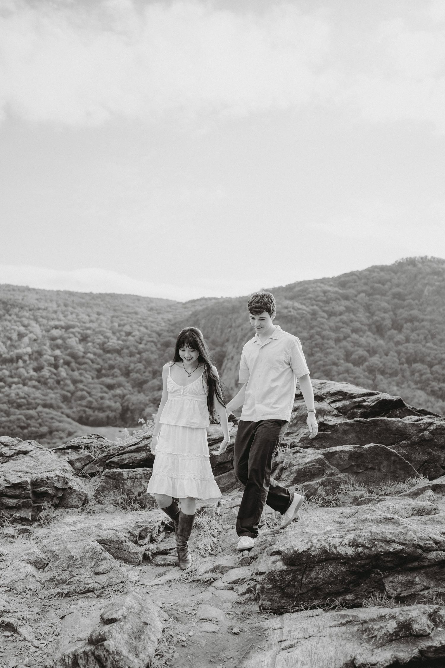 Black and white photo of couple holding hands while walking across rocky terrain with mountain views.