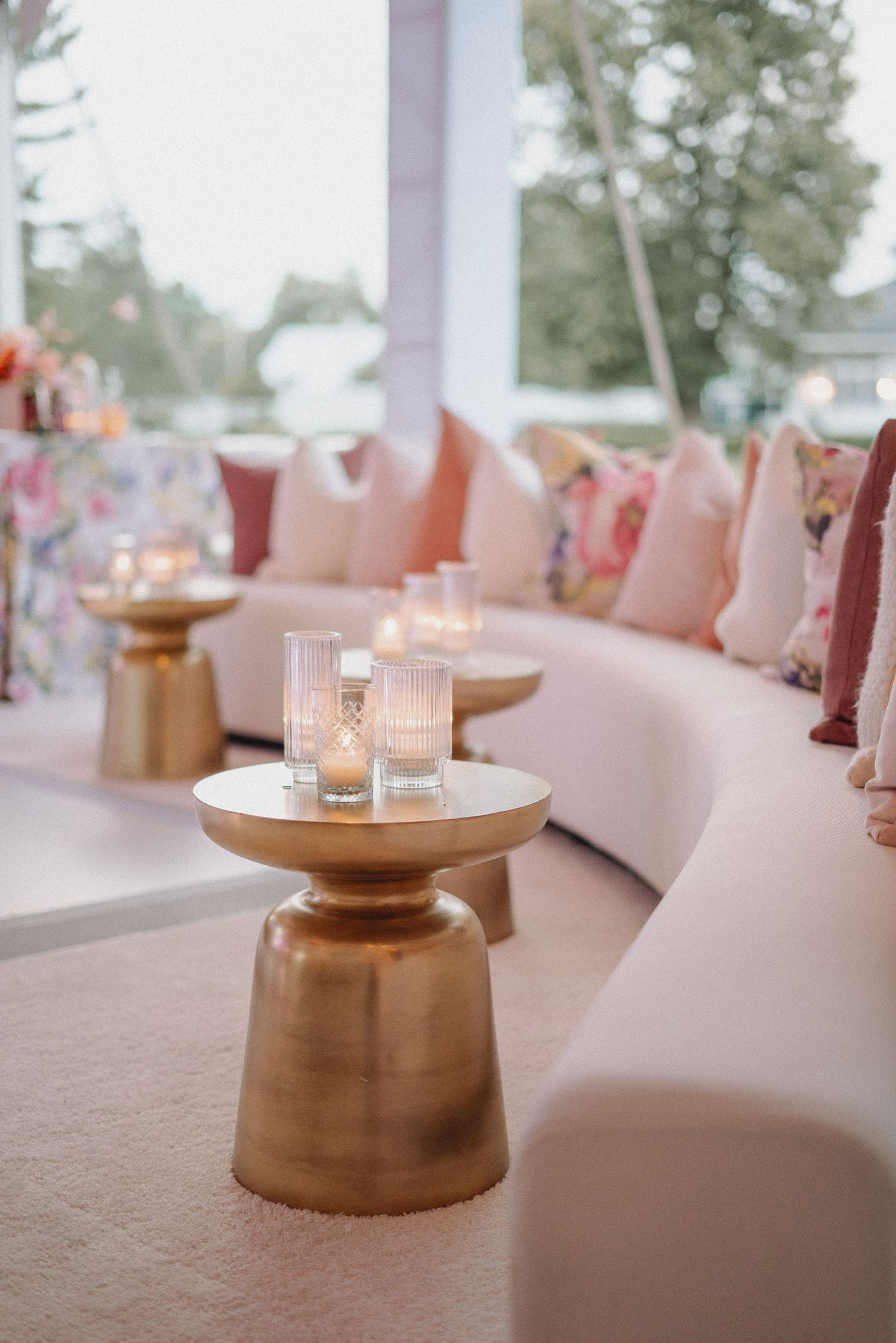 Elegant wedding lounge with curved blush sofa, floral pillows, gold side tables, and glowing candles.