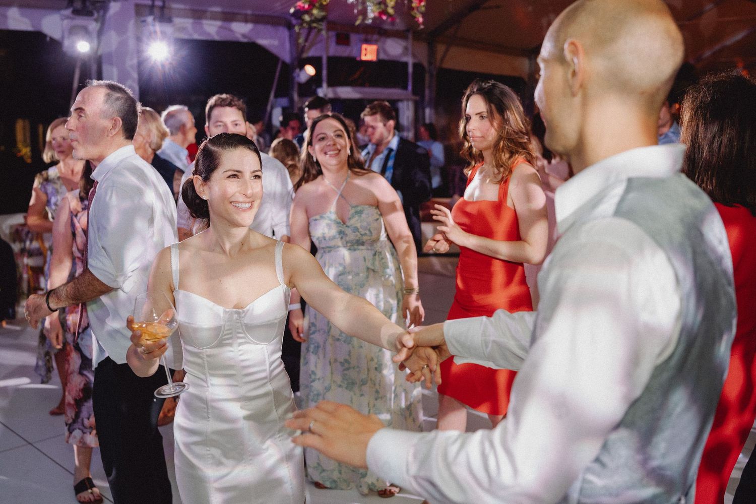 Bride in strapless gown dances joyfully with groom surrounded by guests at lively wedding reception.