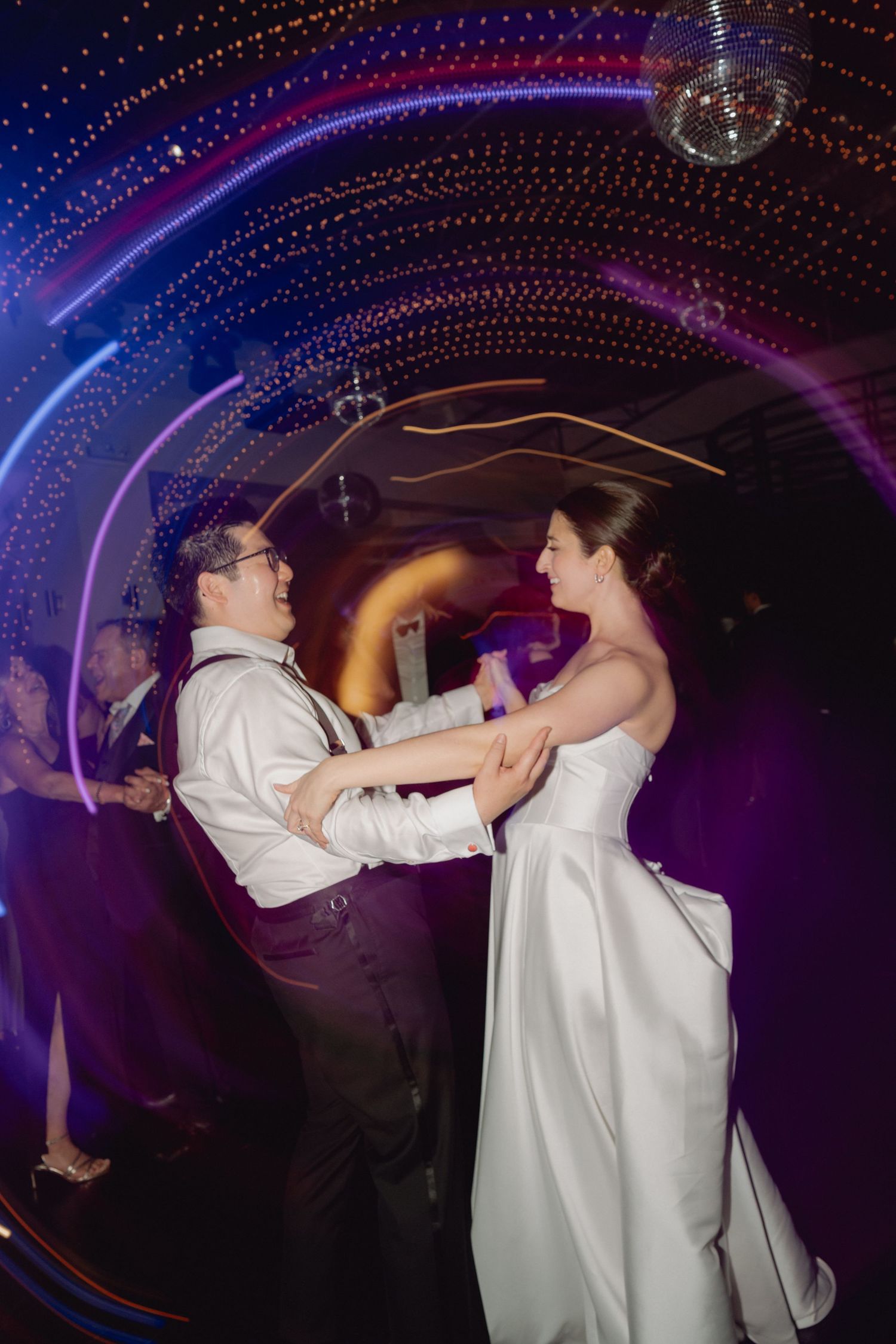 Bride and groom dance joyfully surrounded by swirling colorful lights at their wedding reception.