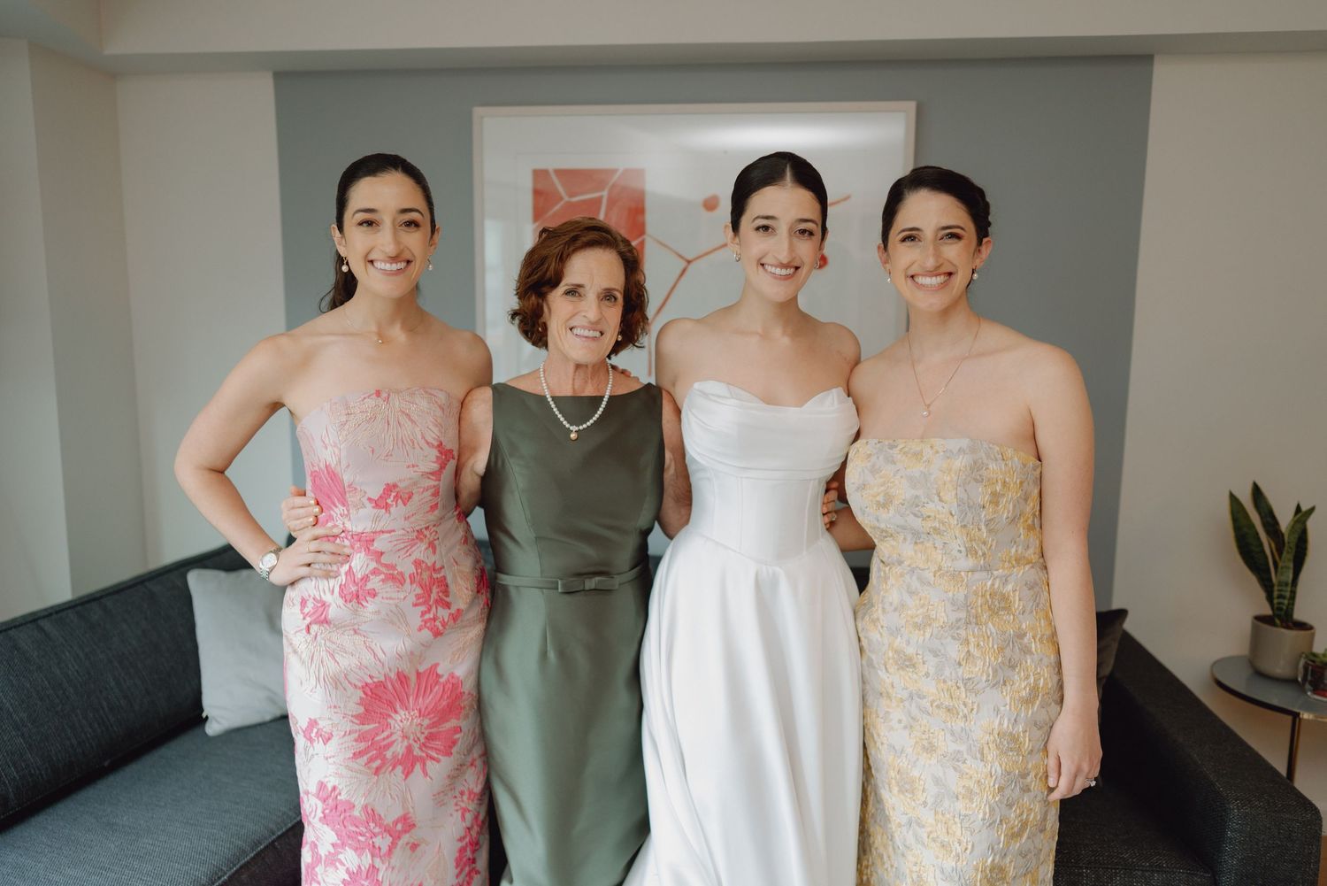 Bride in white strapless gown poses with mother and two sisters in floral dresses before the wedding.