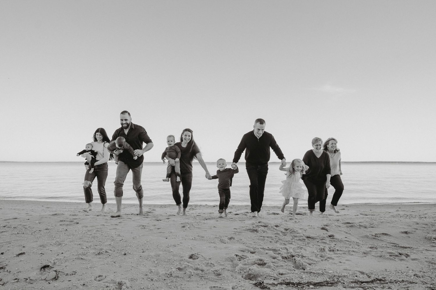 Large family running and laughing together on beach in black and white photo.