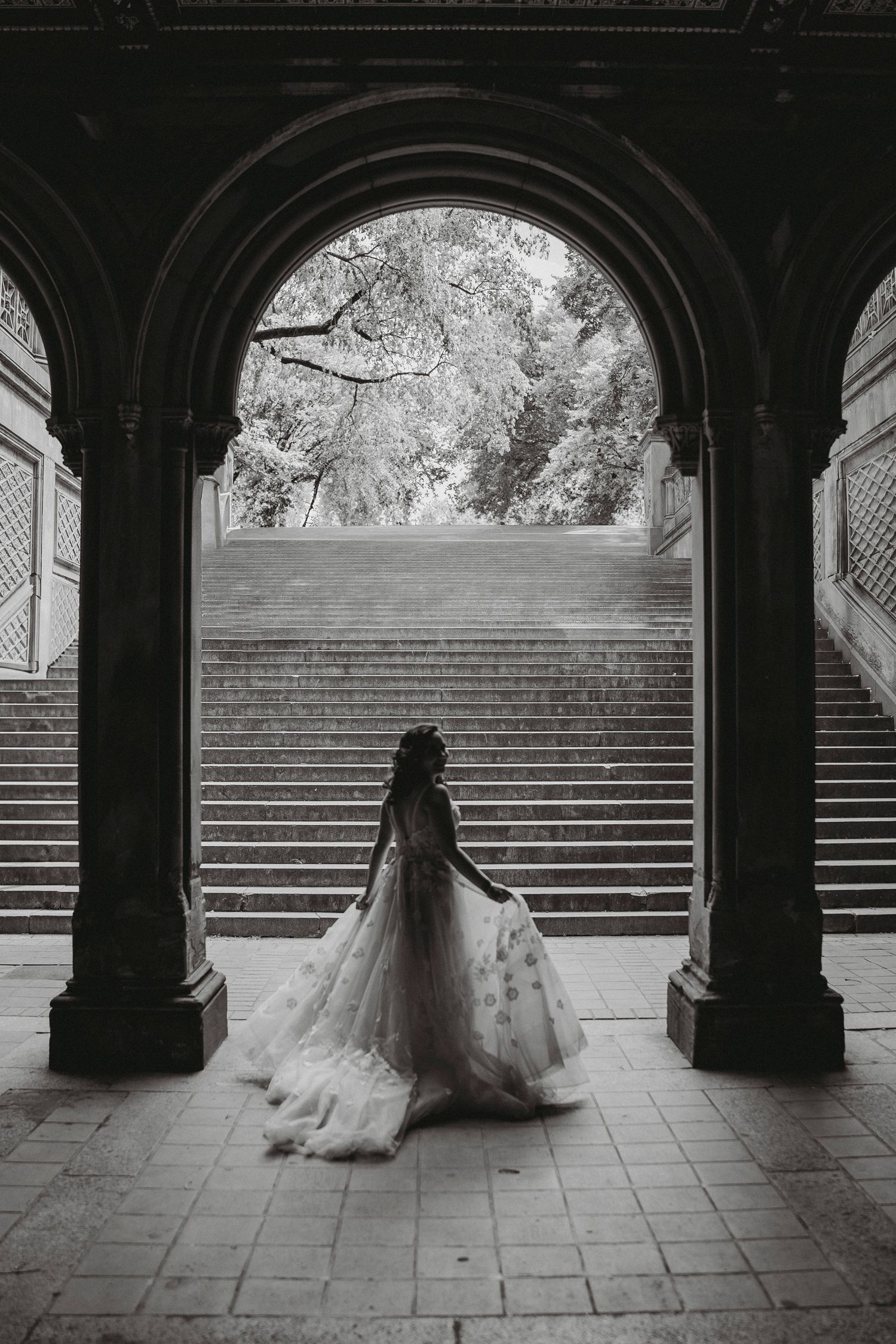 Black and white silhouette of bride in floral gown under stone archway at Bethesda Terrace.