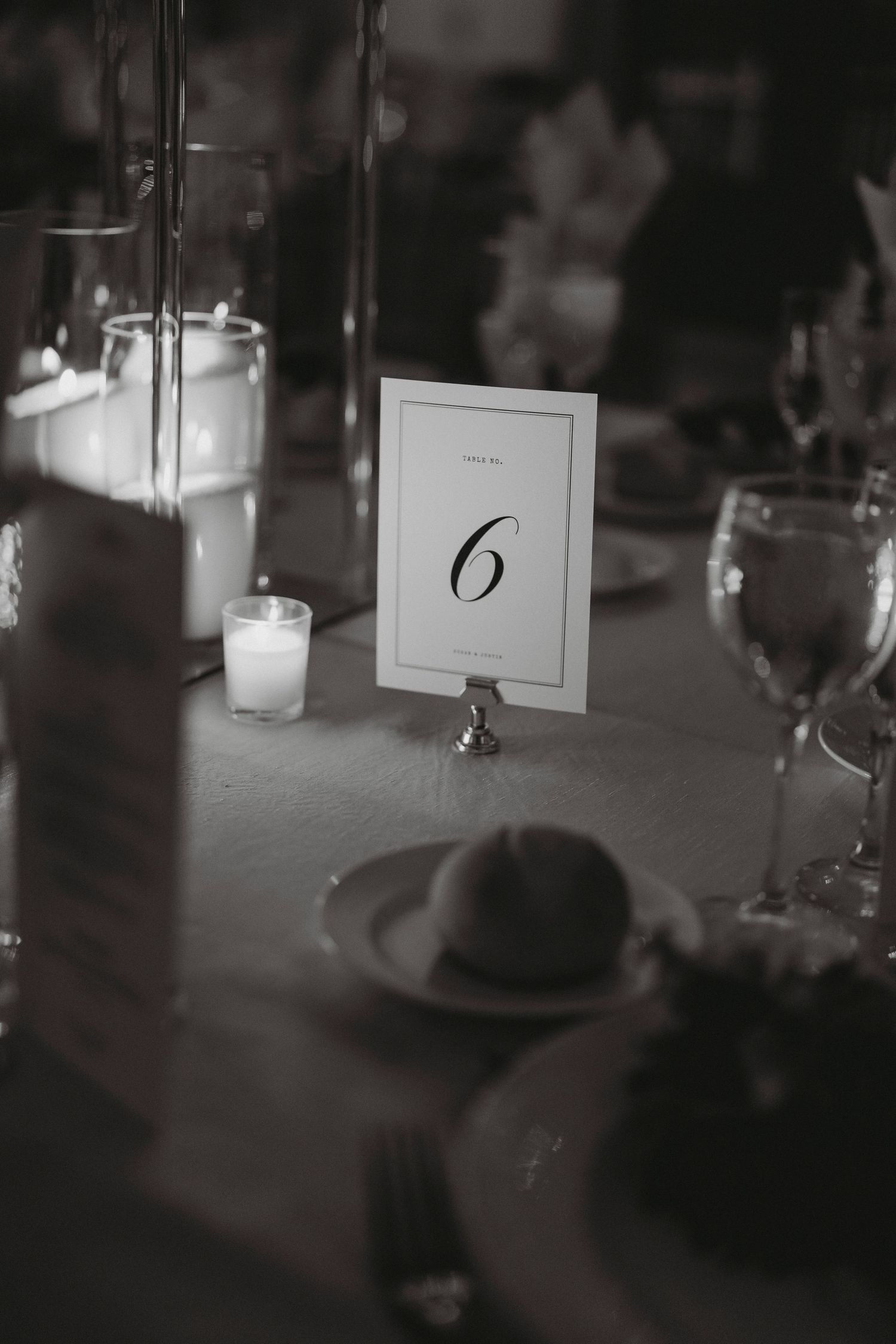 Elegant black and white wedding reception table setting with number six card and candlelight.