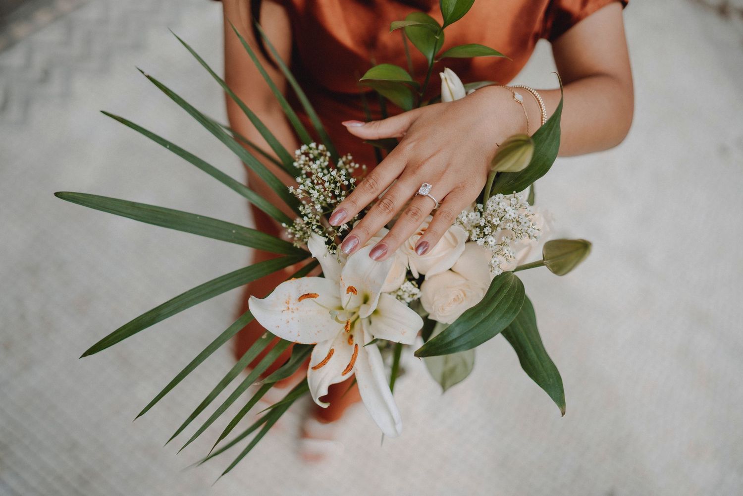 Close-up of bride's hand with engagement ring holding a tropical wedding bouquet with white lilies.