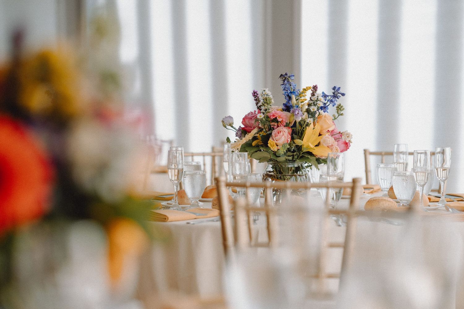 Elegant wedding reception table set with colorful wildflower centerpiece, glassware, and golden chairs.