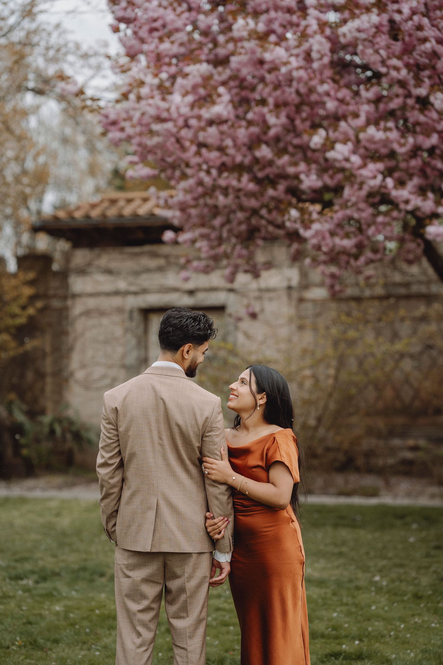 Couple sharing a tender moment in front of blooming pink cherry blossom trees in a garden.