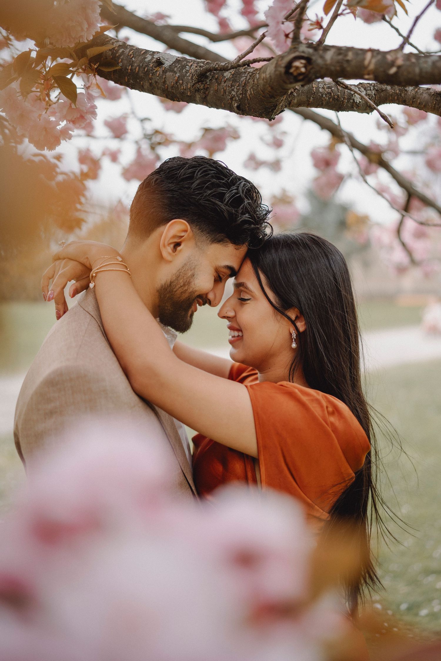 Romantic couple touching foreheads and embracing under blooming pink cherry blossom branches in spring garden.