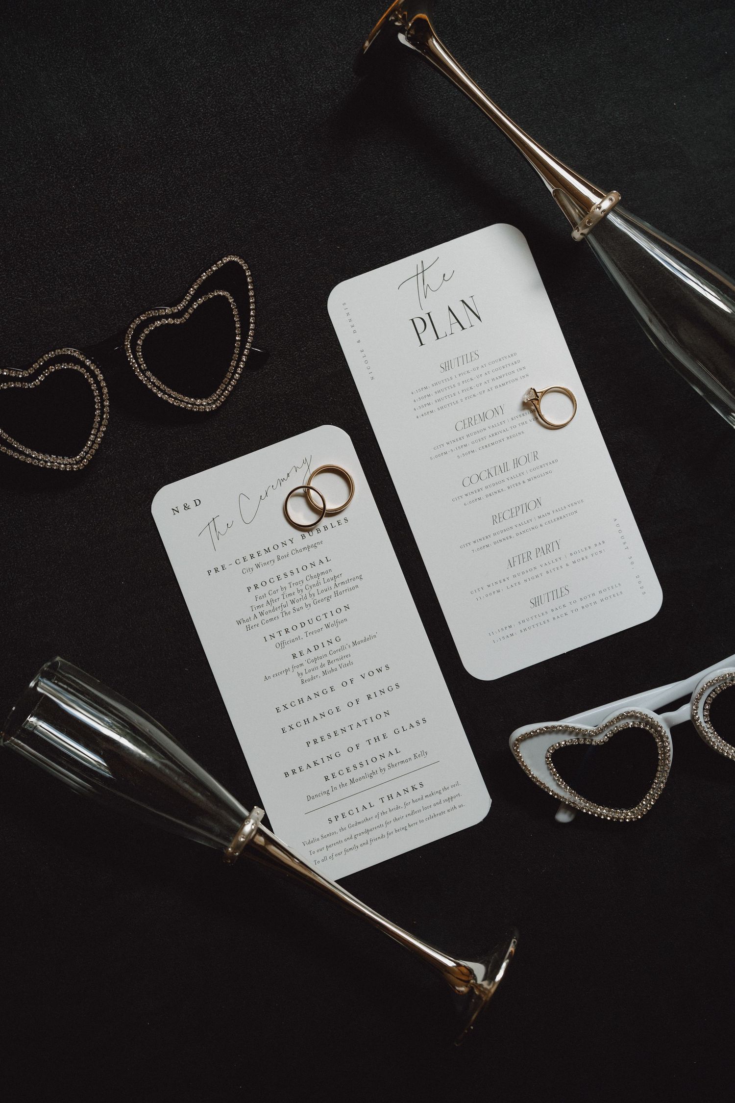 Wedding ceremony programs and reception timeline cards displayed with champagne flutes on black background.