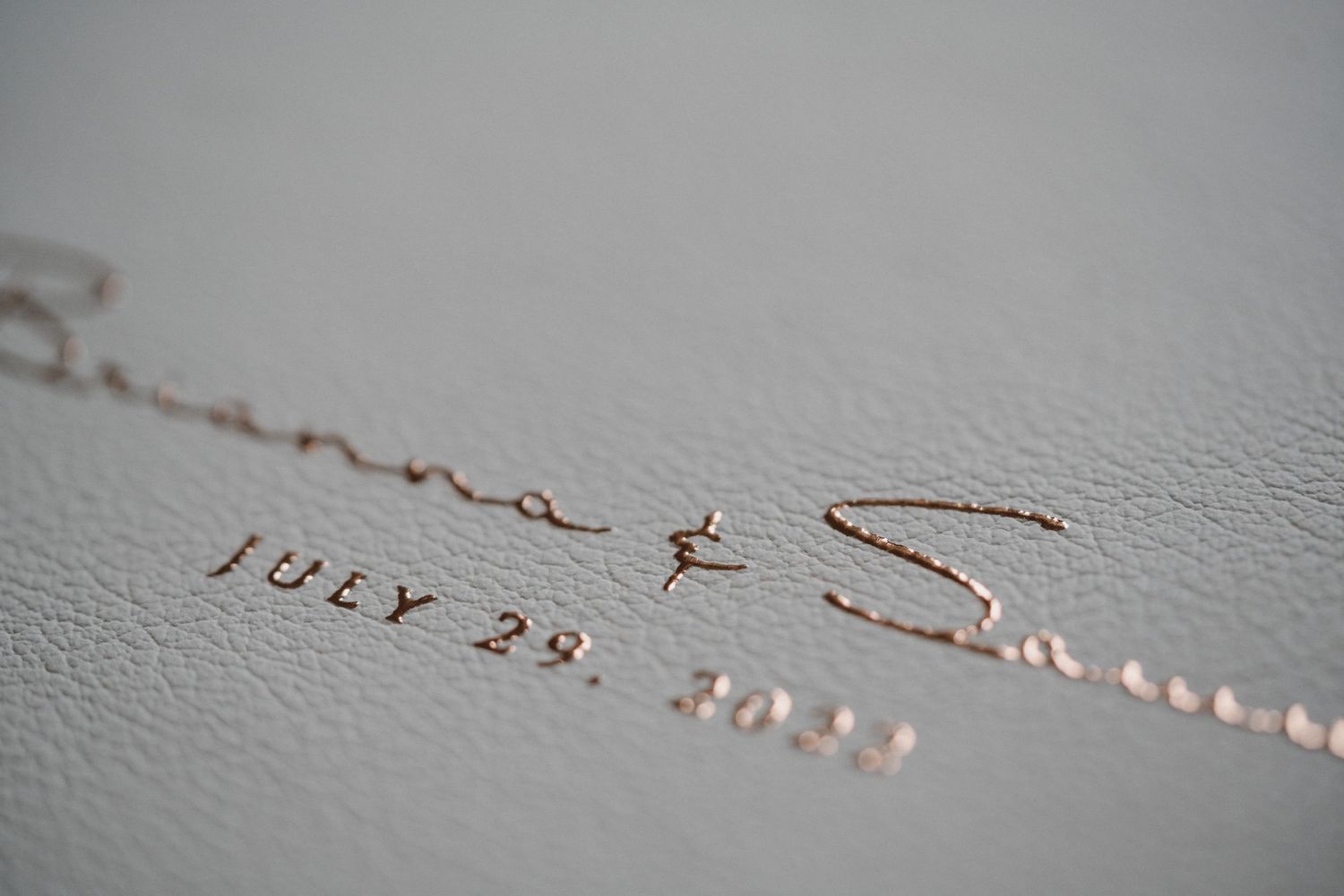 Close-up of rose gold foil stamped names and July 29 date on a gray leather wedding album cover.