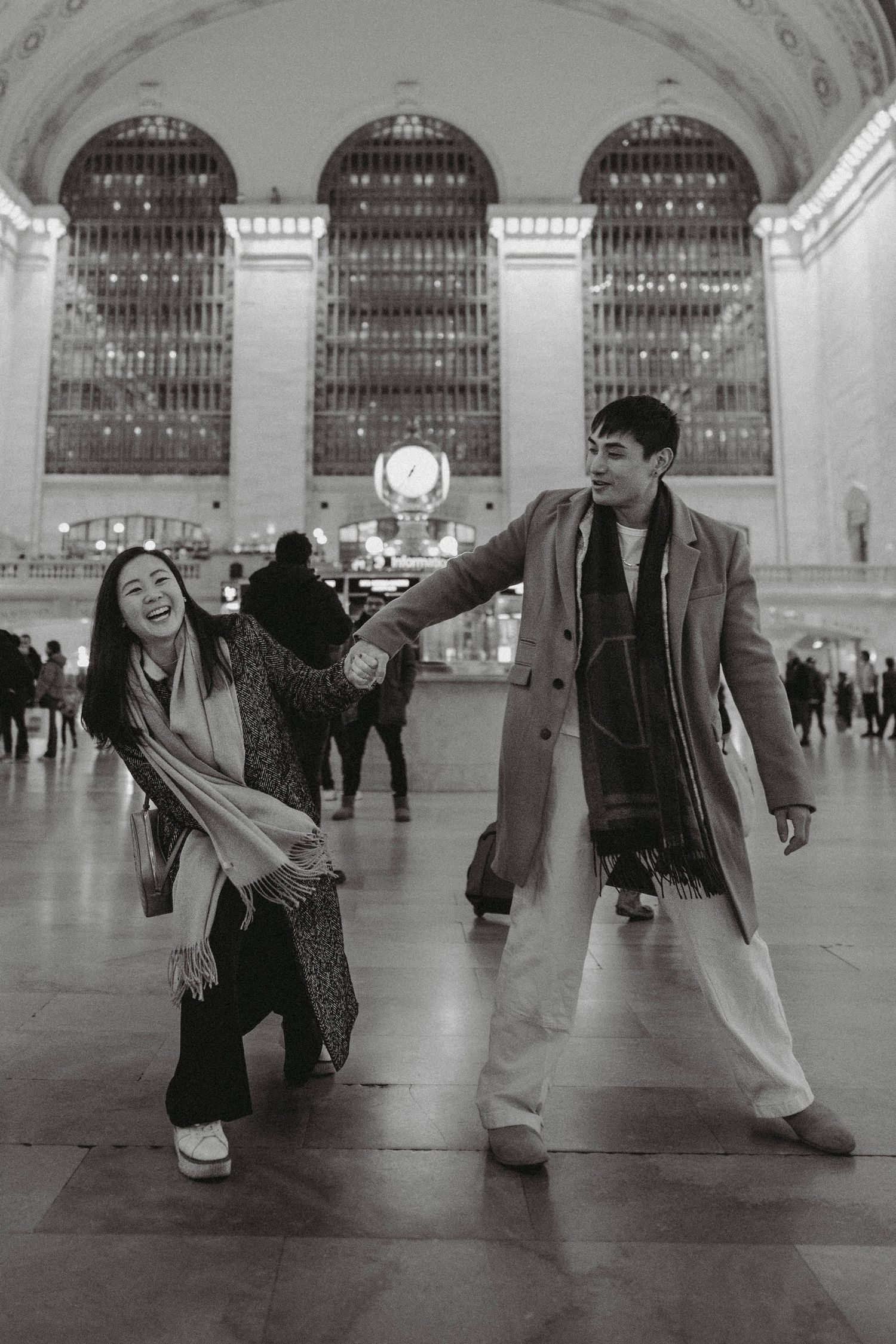 Couple dancing and holding hands in Grand Central Terminal with iconic clock in background.