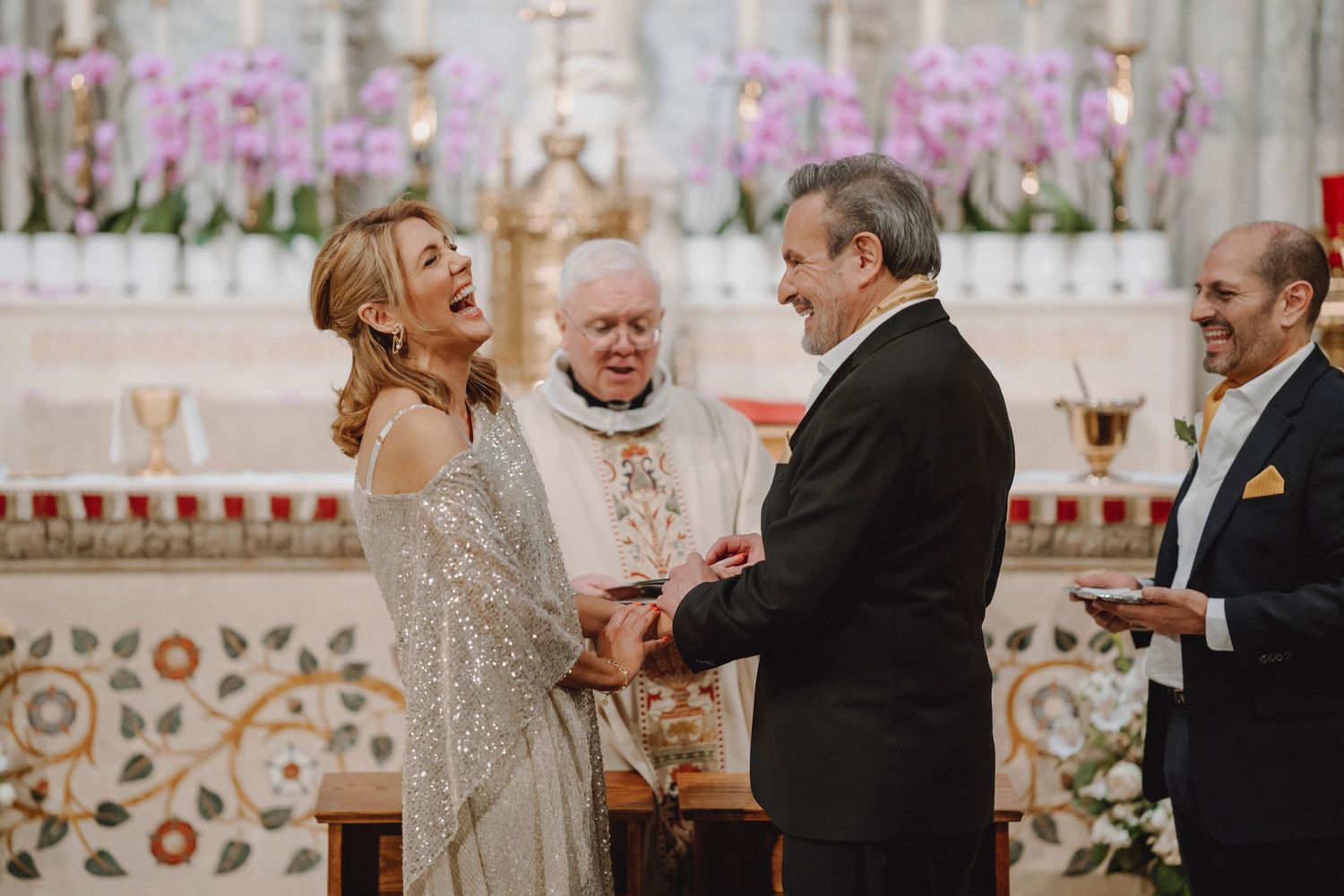 Bride laughing joyfully while exchanging vows with groom before an ornate cathedral altar.