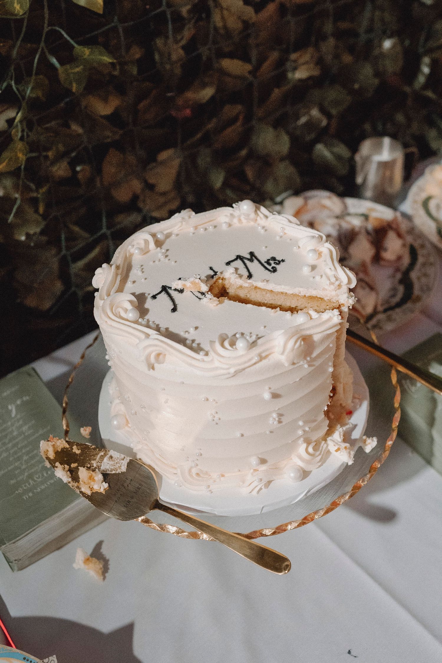 Elegant single-tier white buttercream wedding cake with script lettering and gold cake server on display.