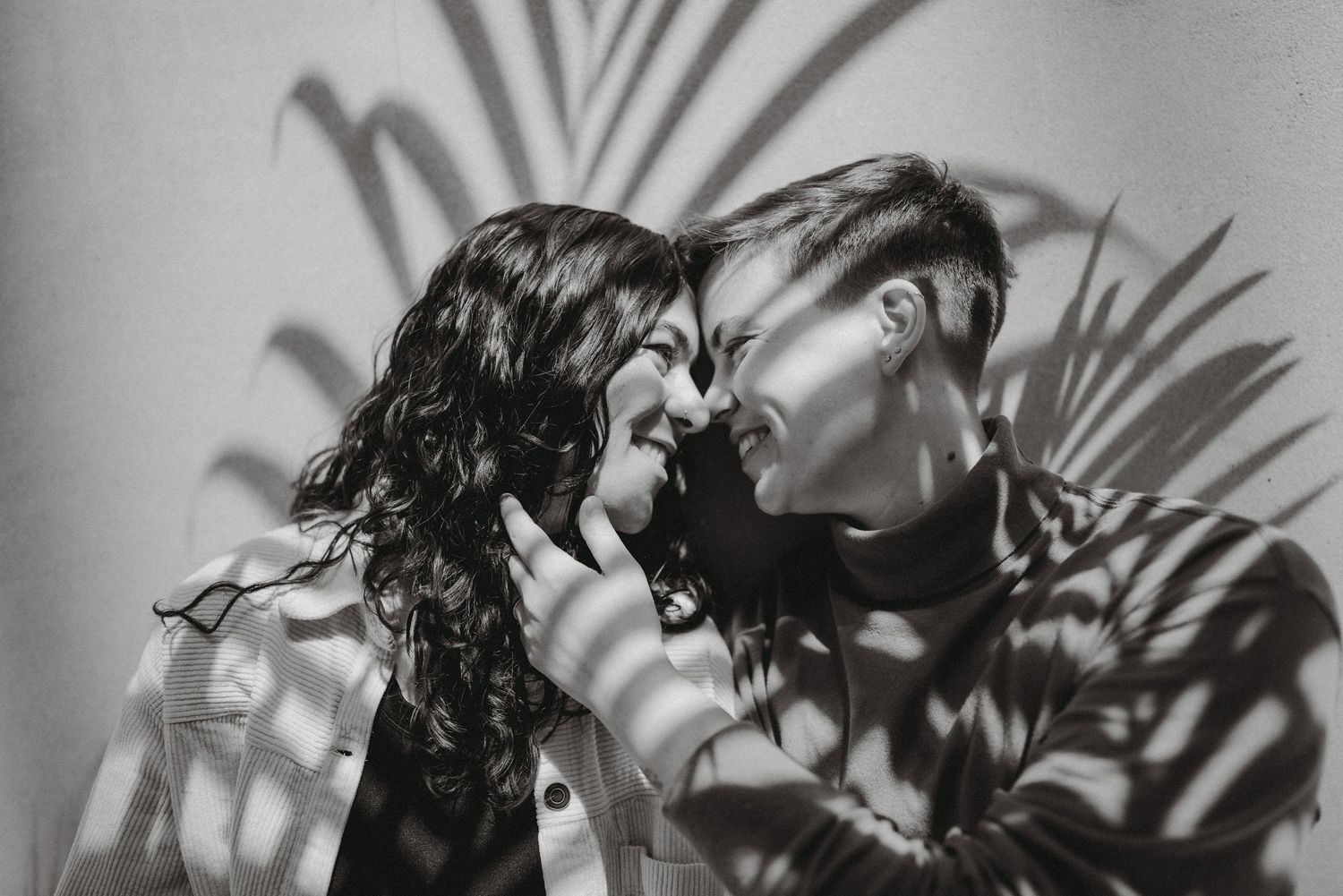 Black and white photo of a couple smiling at each other with palm leaf shadows.
