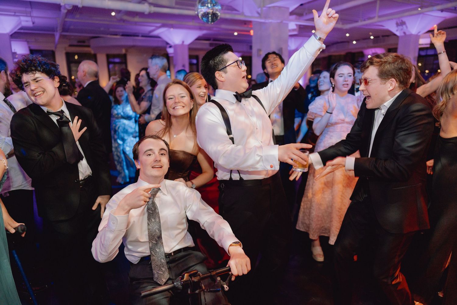 Groom celebrates with friends on the wedding dance floor, including a guest in a wheelchair.