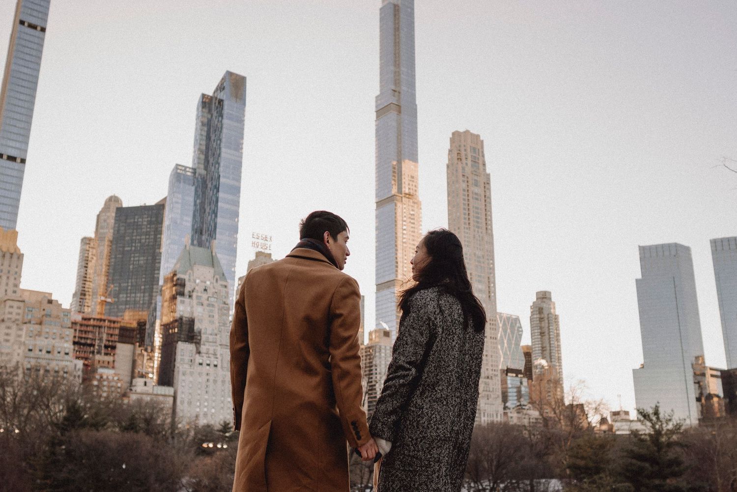 Couple holding hands while gazing at the stunning New York City skyline from Central Park in winter.