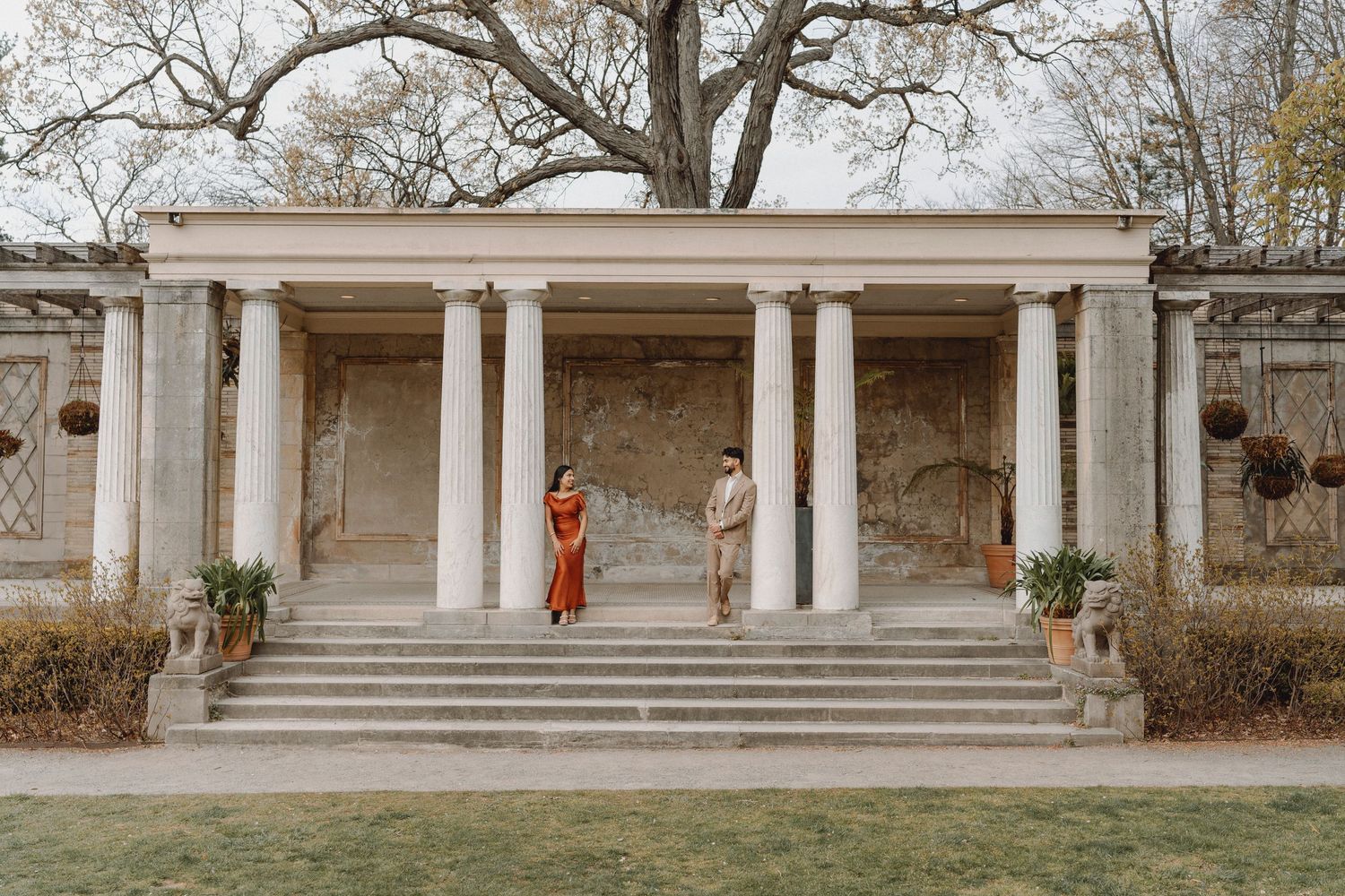 Couple walking down steps of a classical stone colonnade building surrounded by bare trees.