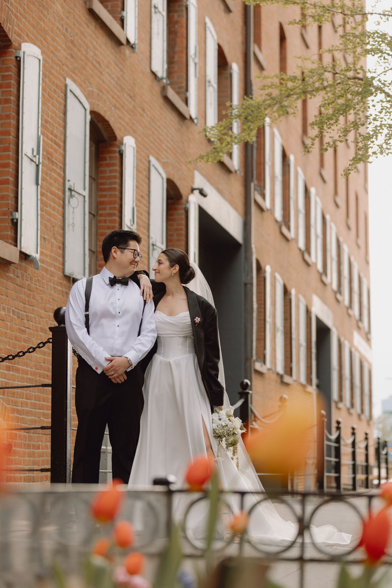 Bride and groom share a romantic moment outside red brick building with tulips in the foreground.