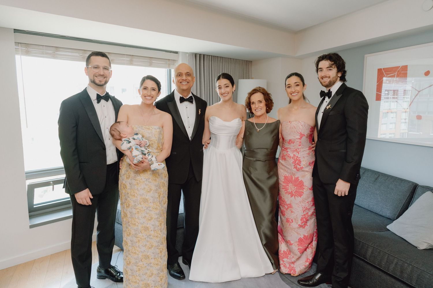 Wedding party group photo with bride in white gown surrounded by family in formal attire.