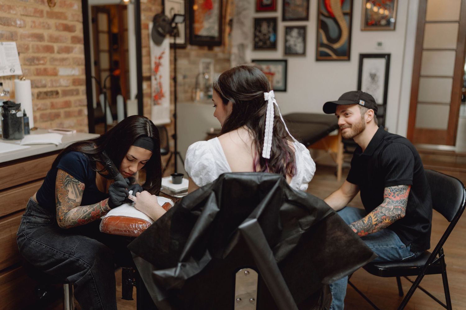 A woman gets a tattoo in a vibrant tattoo studio while two tattooed artists work together.