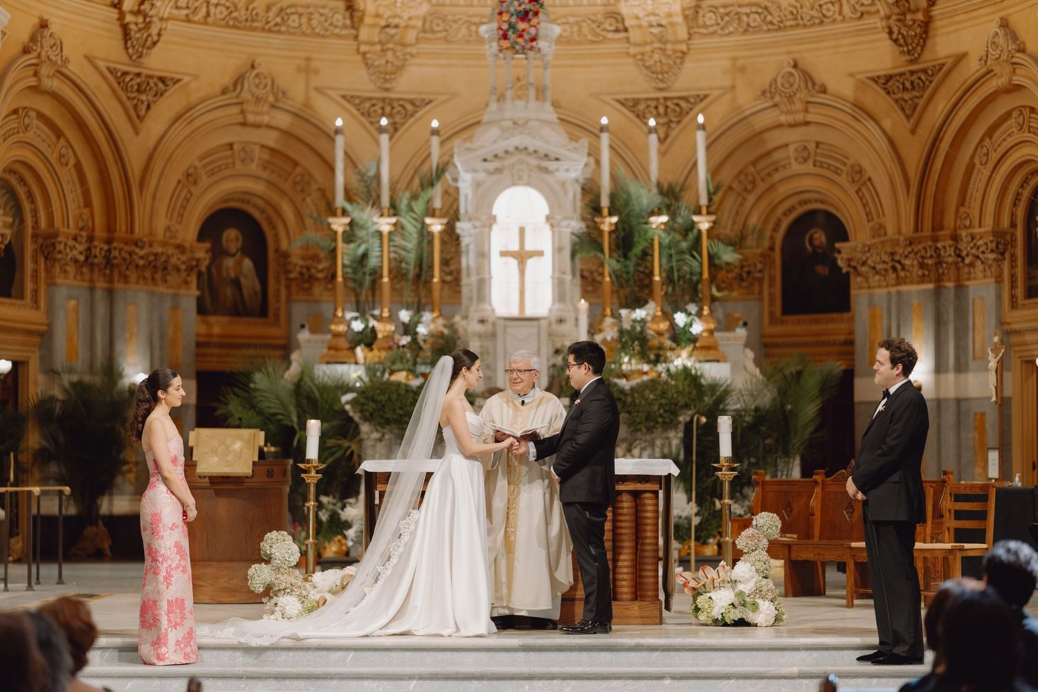 Bride and groom exchanging vows at ornate church altar with candles and floral arrangements.