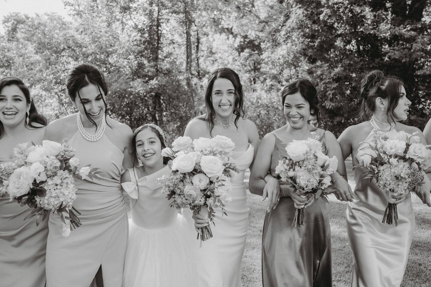 Black and white photo of smiling bride with bridesmaids holding bouquets outdoors.