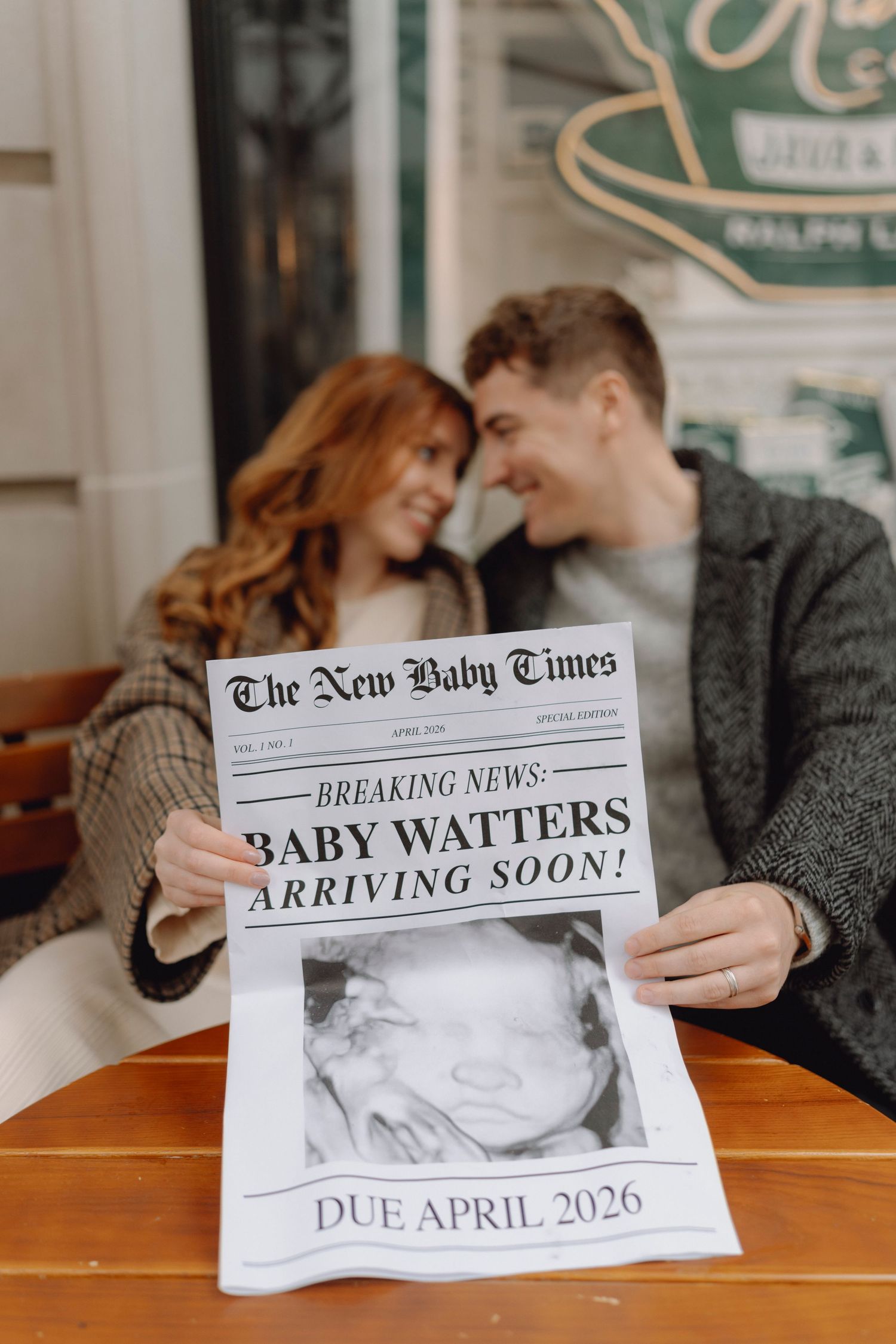 Smiling couple holding New Baby Times newspaper announcing Baby Watters due April 2026.