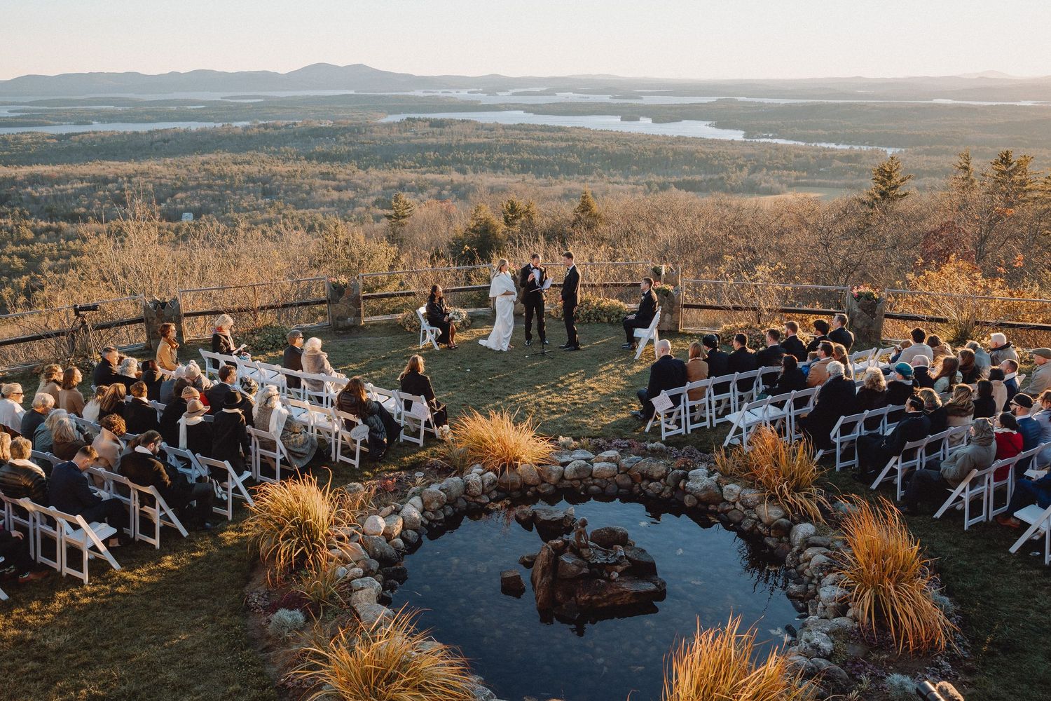 Aerial view of an intimate hilltop wedding ceremony with a stone pond and stunning autumn landscape.