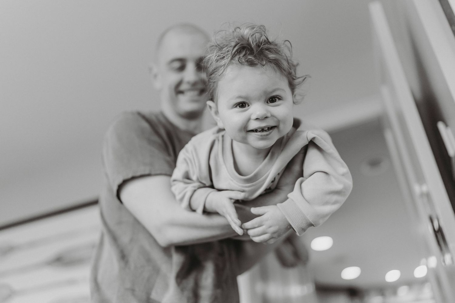 Black and white photo of smiling bald father holding happy curly-haired baby.