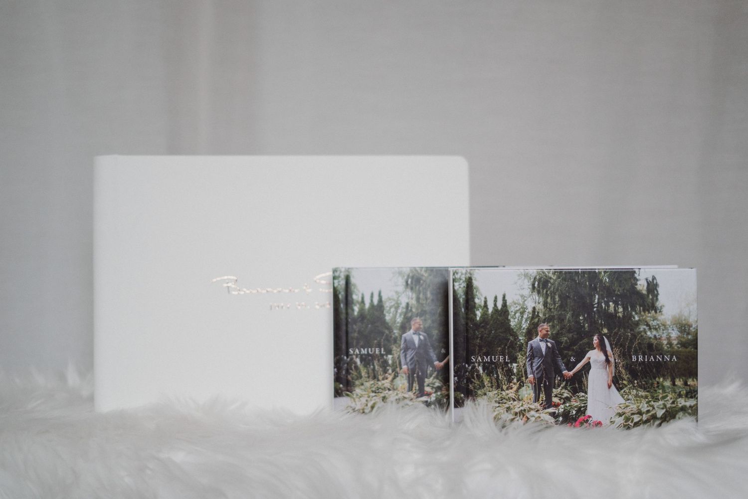 Elegant wedding photo albums with custom covers displayed on white fur, showcasing a couple's special day.