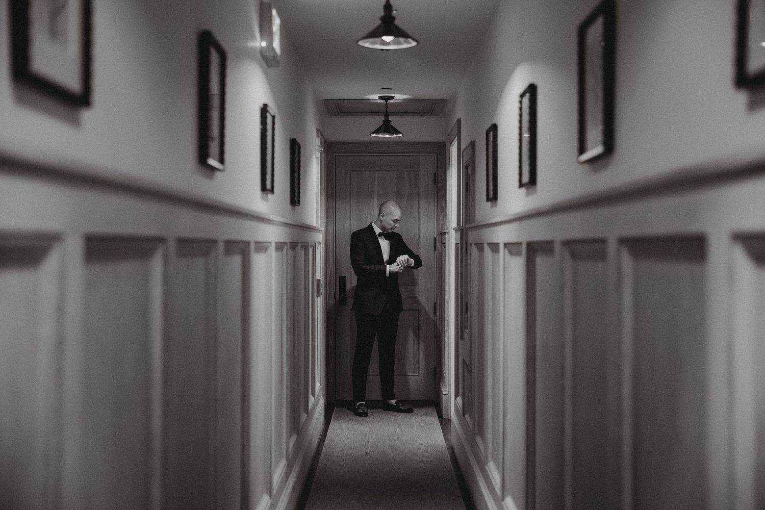 Black and white photo of a dapper groom standing alone in an elegant hallway before his wedding.