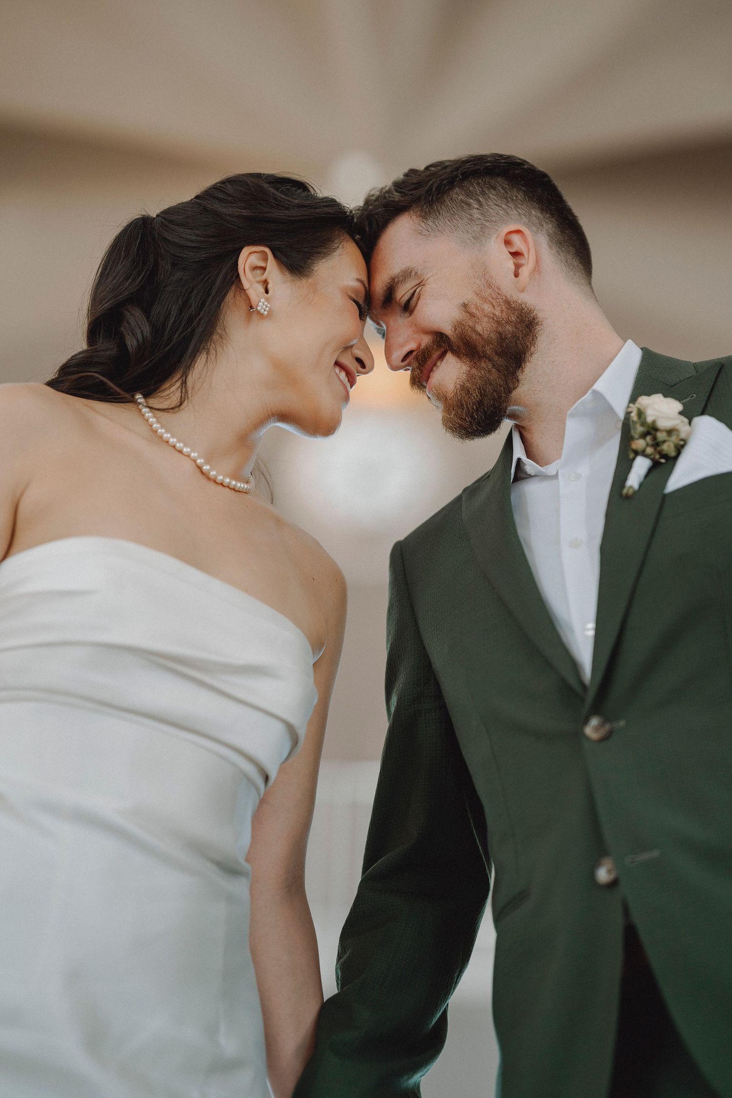 Smiling bride and groom touch foreheads tenderly in a romantic color wedding portrait.
