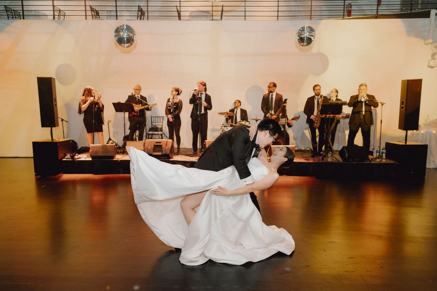 Bride and groom share a romantic dip dance in front of a live band at their wedding reception.