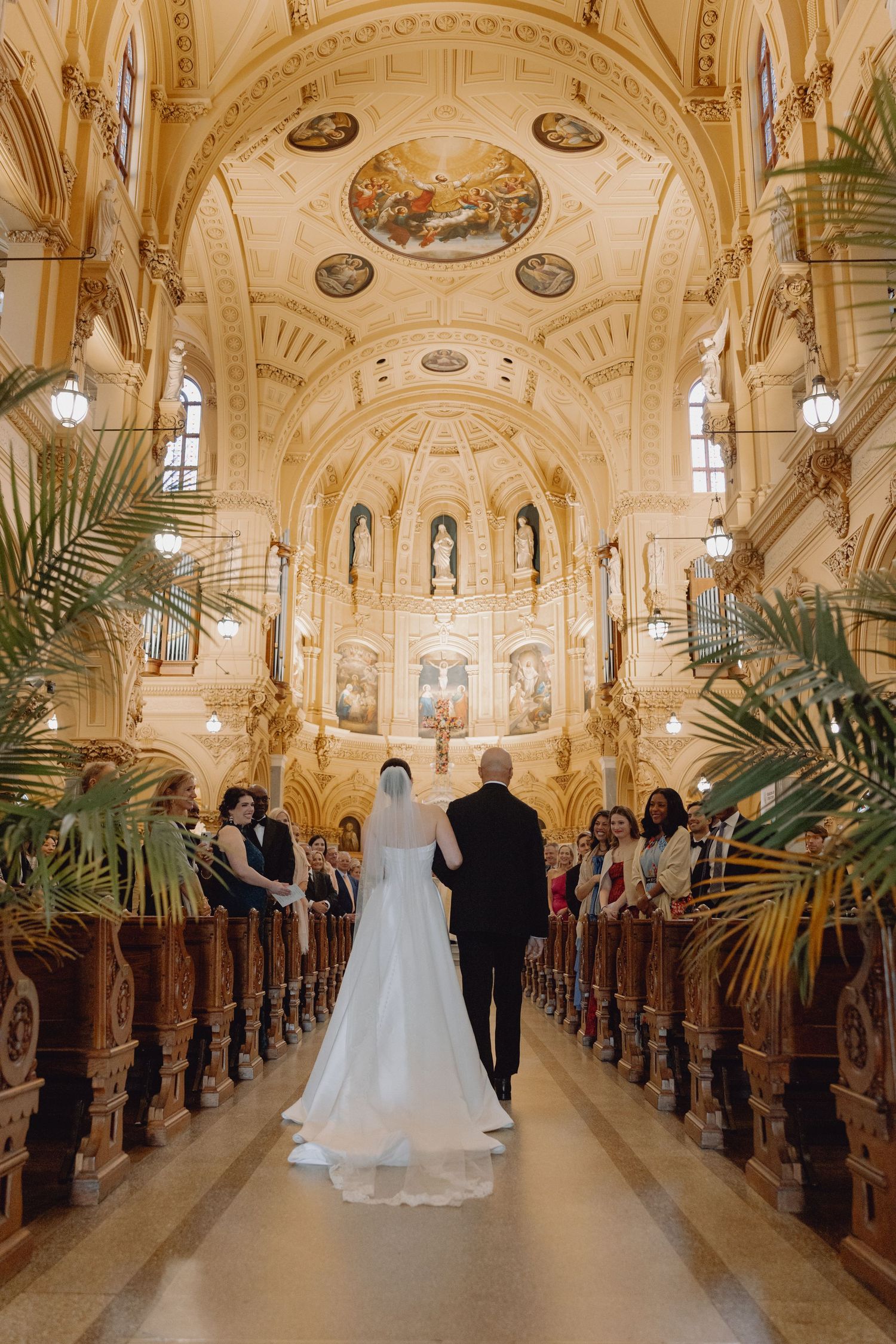 Bride walking down ornate church aisle with escort in stunning gold cathedral wedding ceremony.