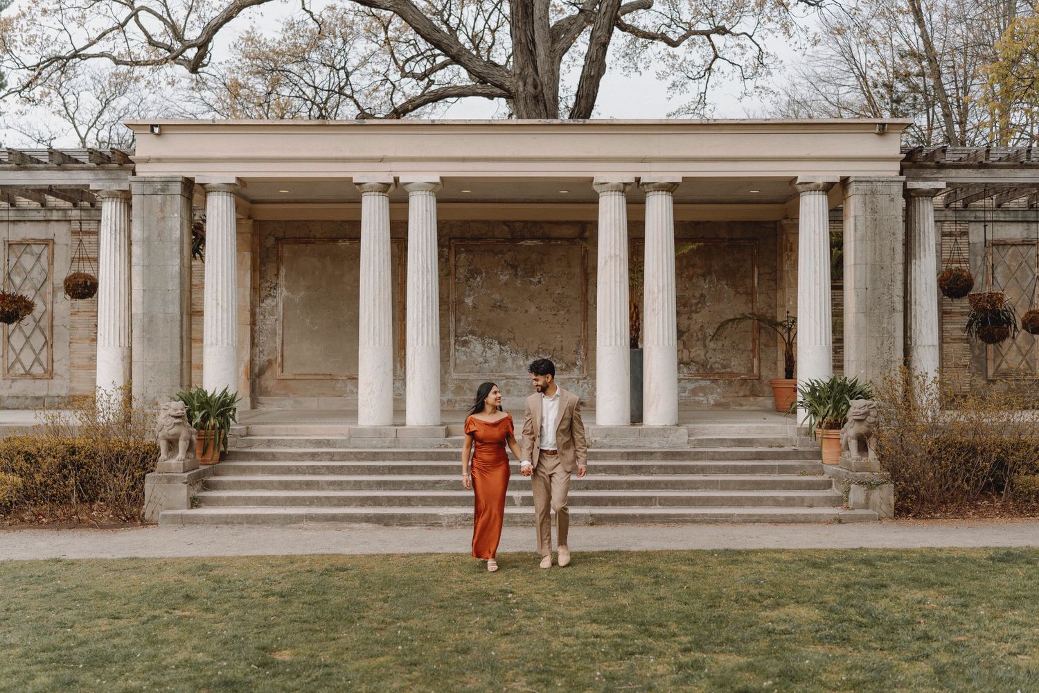 Engaged couple holding hands in front of a grand neoclassical building with white columns.