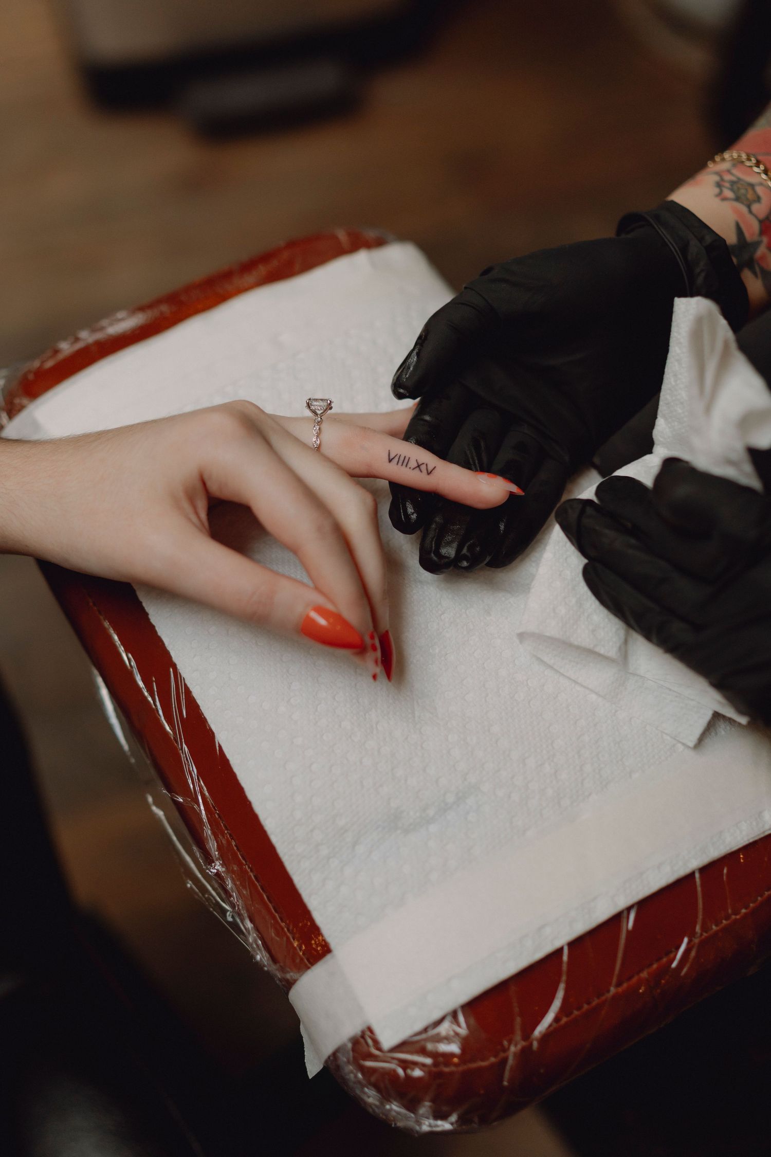 Tattoo artist in black gloves carefully applying a small finger tattoo on a client's hand.