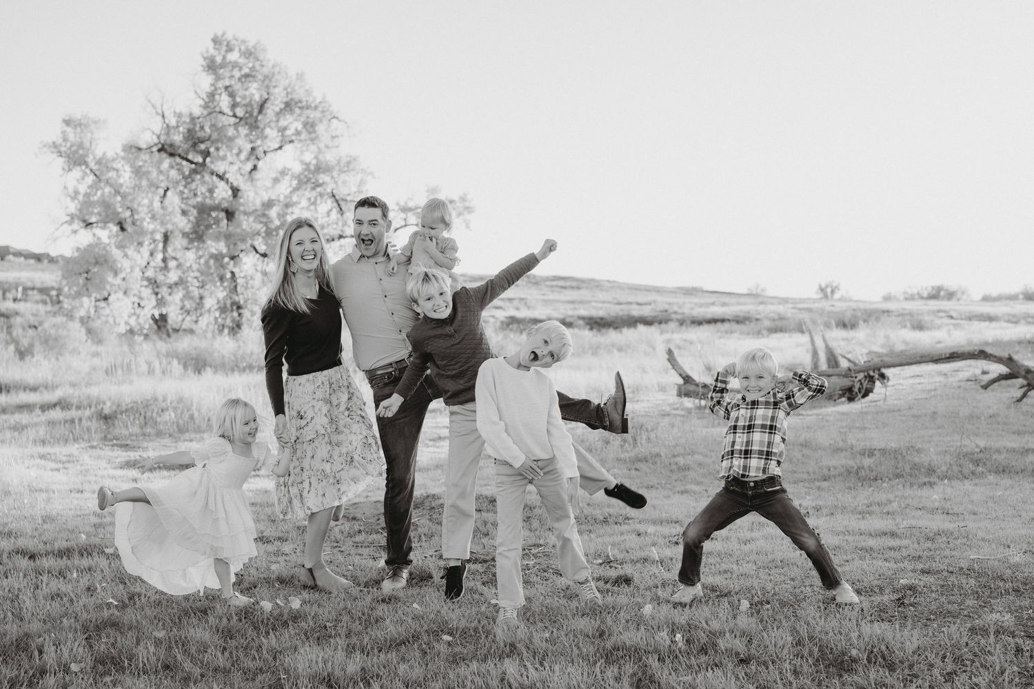 Playful black and white family photo with children jumping in an outdoor field.