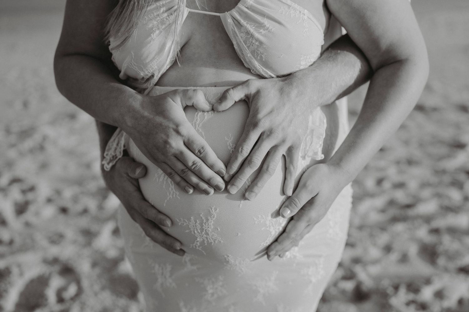 Black and white photo of couple forming heart shape with hands on baby bump.