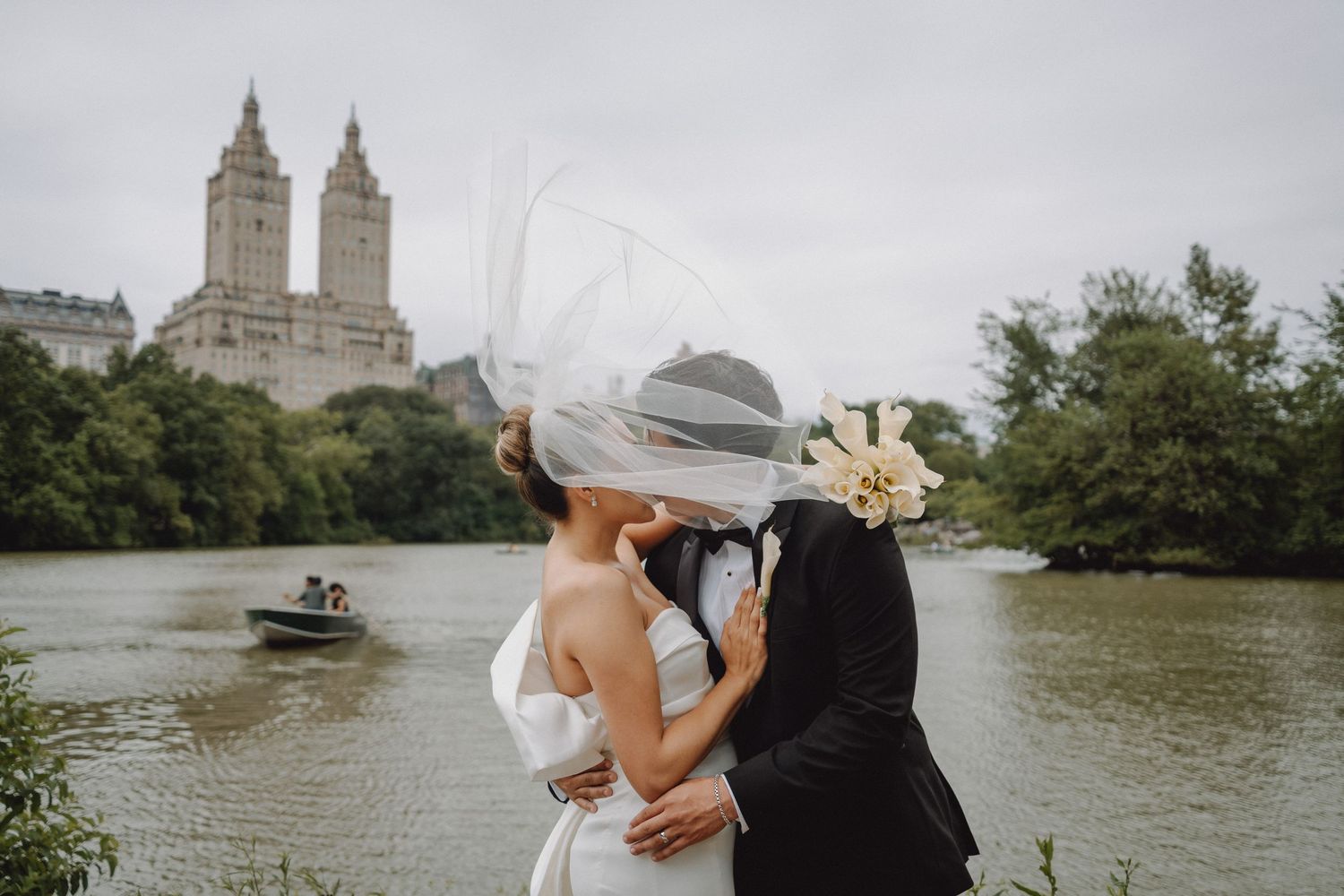 Bride and groom sharing a kiss by the lake in Central Park with iconic buildings behind.