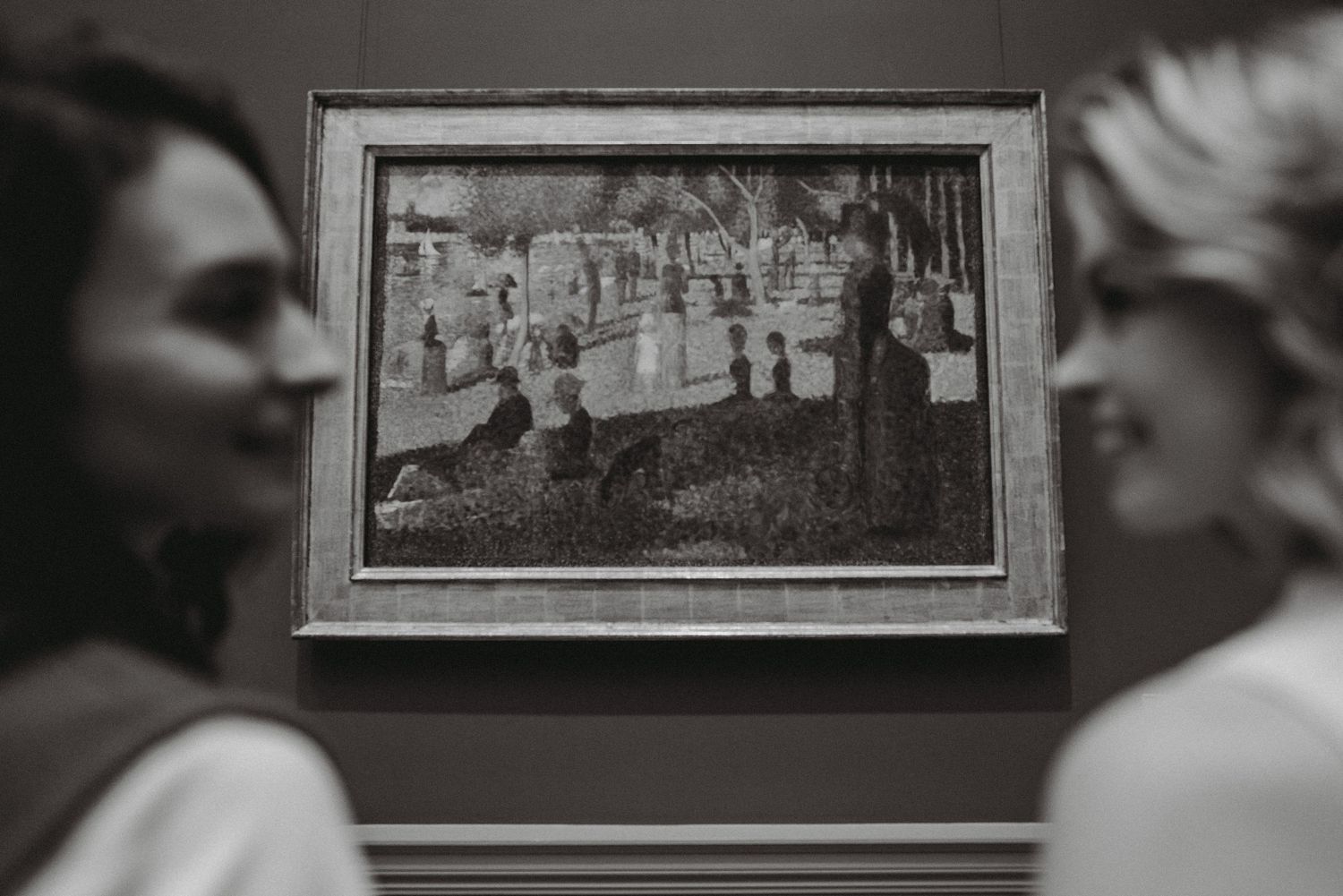 Black and white photo of two women admiring Georges Seurat painting in an art museum.