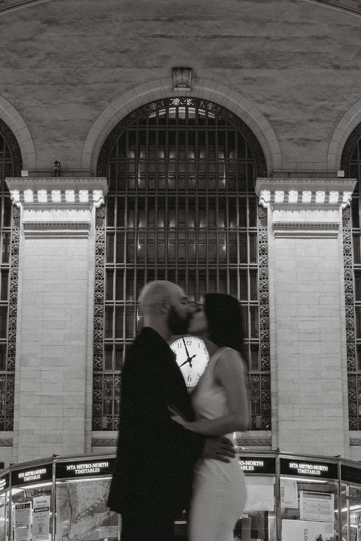 Blurred artistic black and white photo of couple kissing under Grand Central Terminal clock.