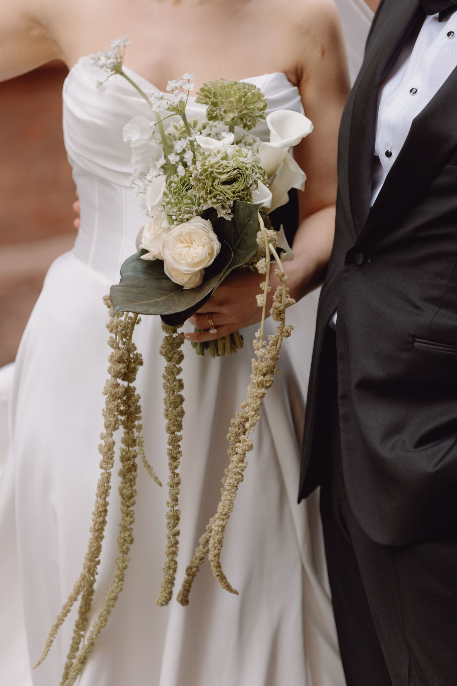 Bride holds elegant cascading bouquet with white roses, calla lilies, and trailing amaranthus on wedding day.
