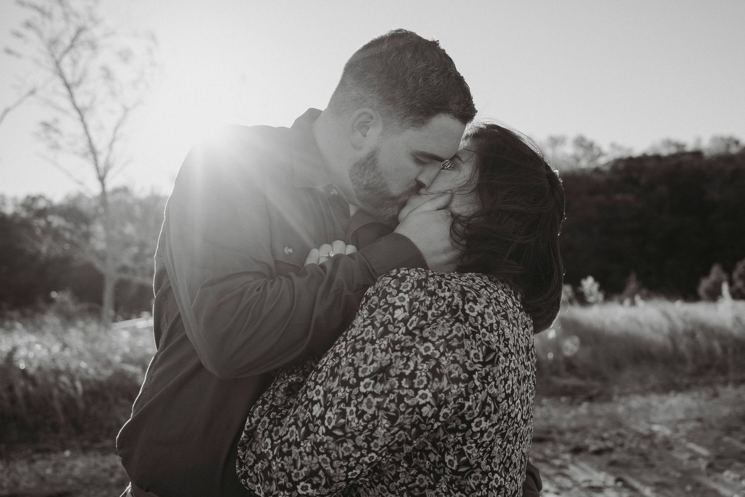 Black and white romantic photo of couple sharing a kiss in bright sunlit outdoor setting.