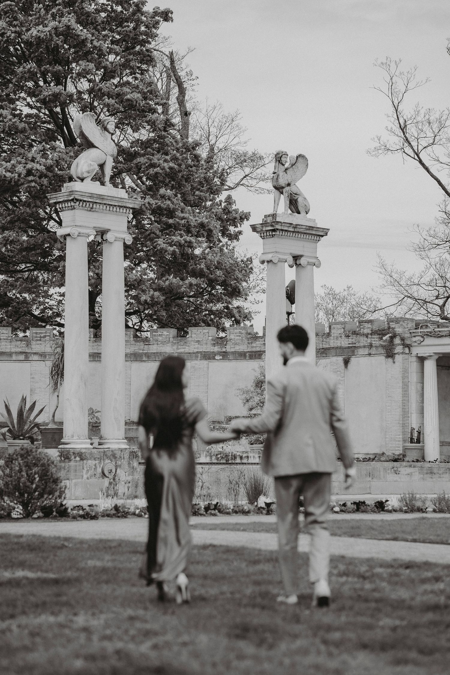 Black and white photo of couple walking toward ornate columns topped with griffin statues.