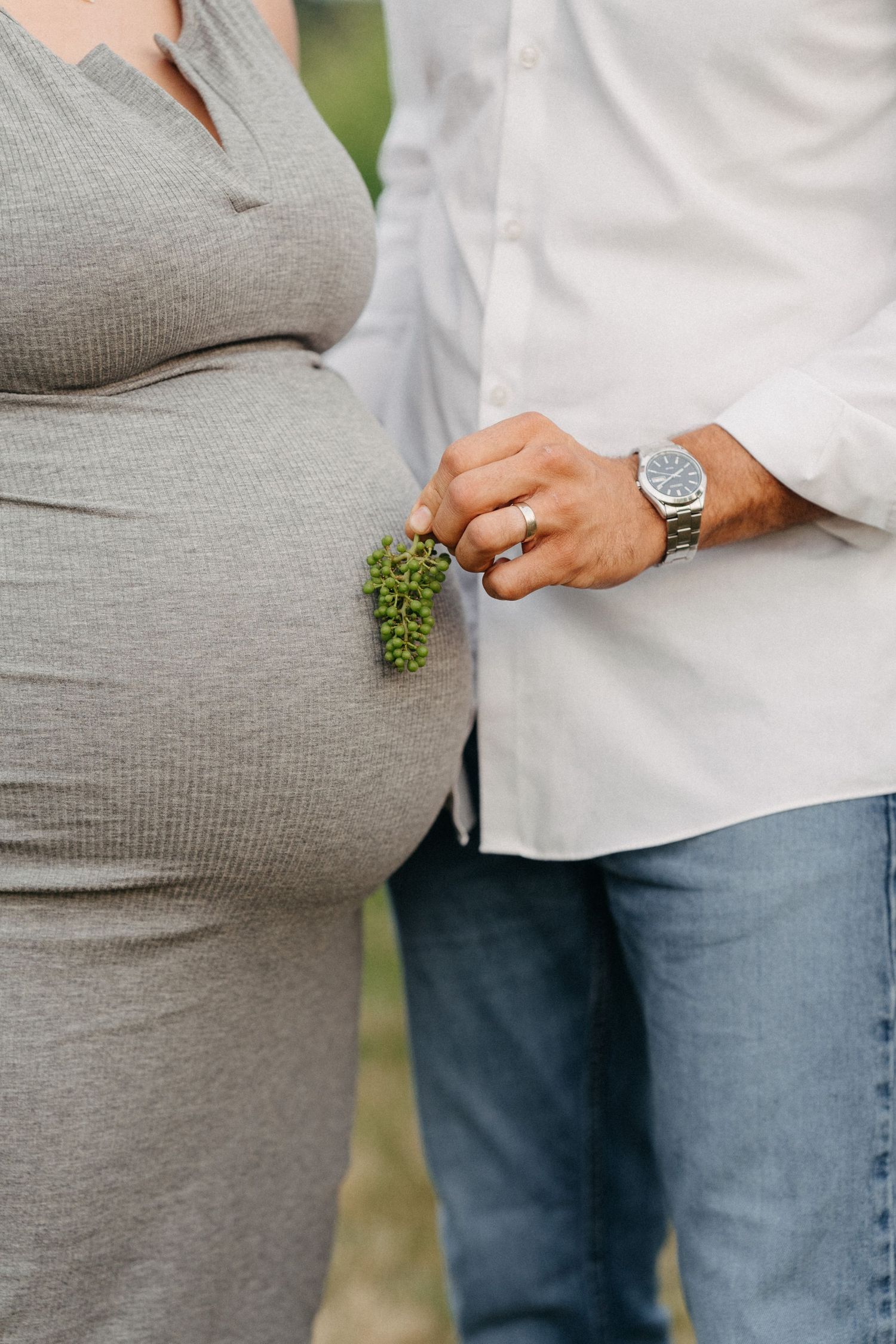 Close-up of pregnant belly with man holding greenery.