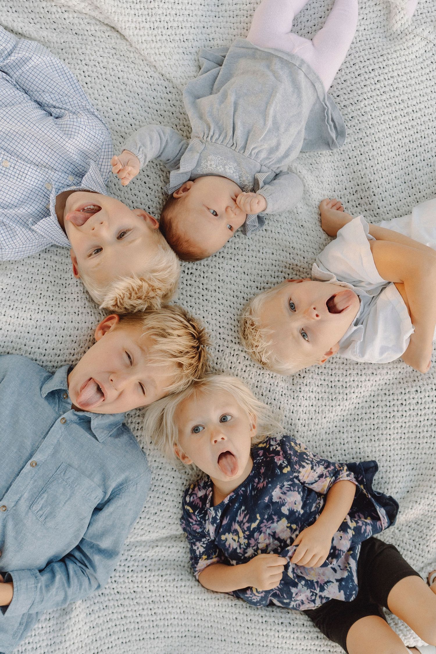 Five young children lying in a circle on a light blanket making funny faces.