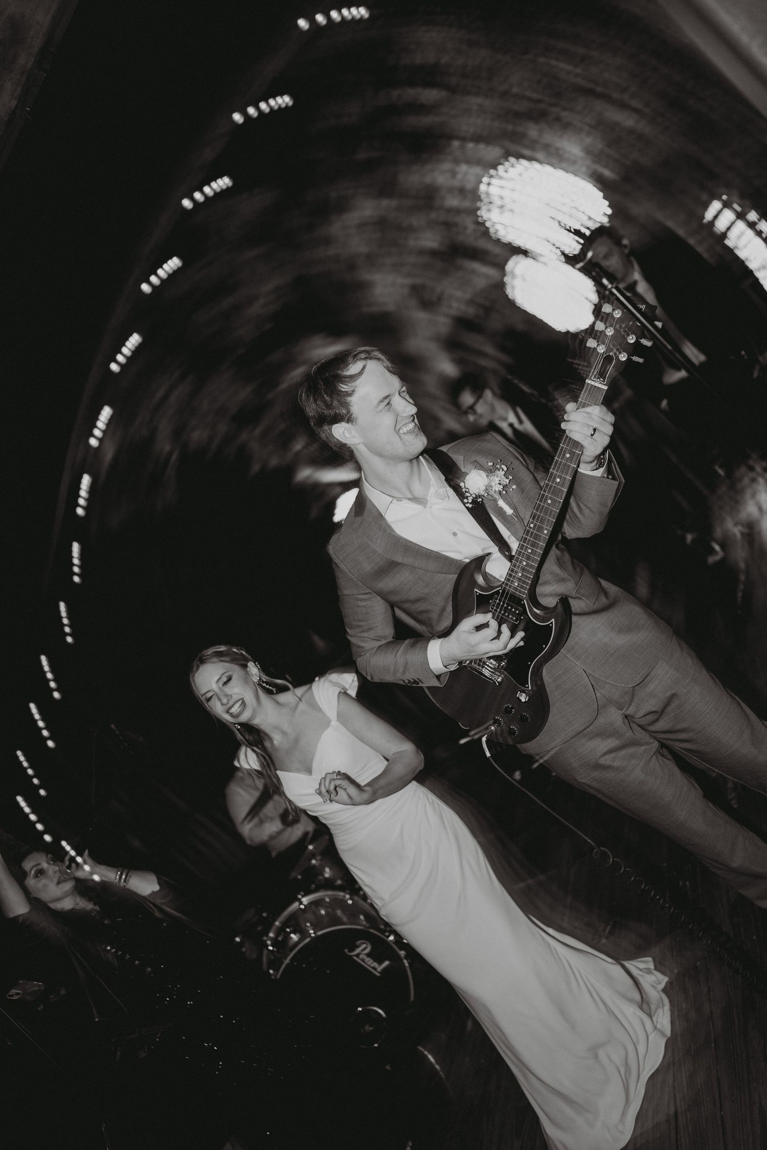 Dynamic black and white photo of groom playing guitar with bride on dance floor.