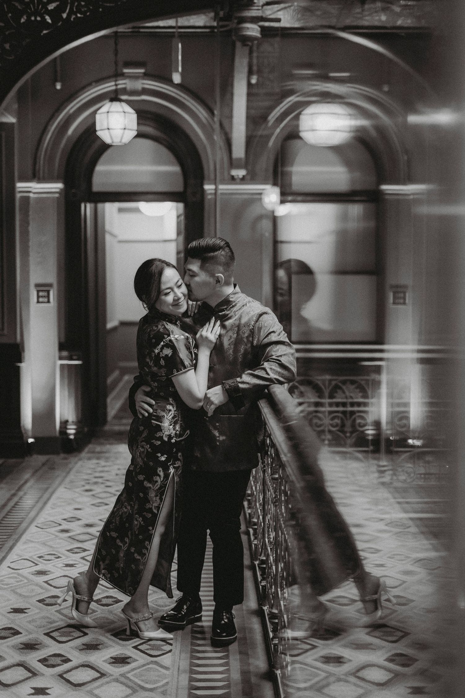 Romantic couple in elegant traditional Chinese qipao and suit sharing a tender moment in a grand hallway.