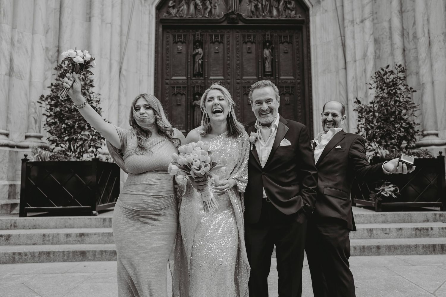 Black and white photo of bride laughing with wedding party on church steps.
