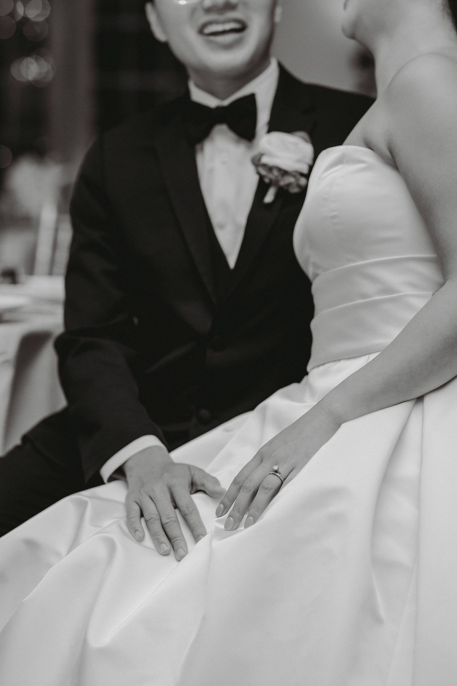 Bride and groom hold hands during wedding reception, showing off wedding rings in elegant black and white photo.